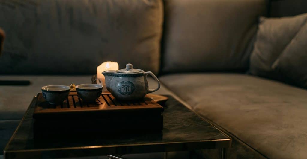 A tea set is arranged on a table in a dimly lit room with a couch.