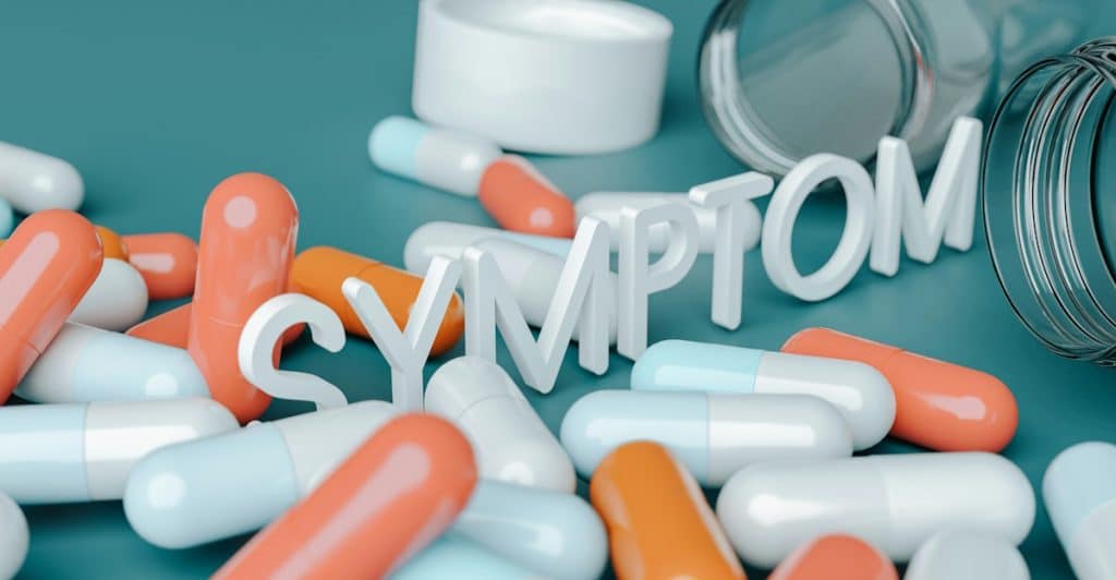 White block letters spelling the word SYMPTOM scattered amongst various colorful medication capsules.