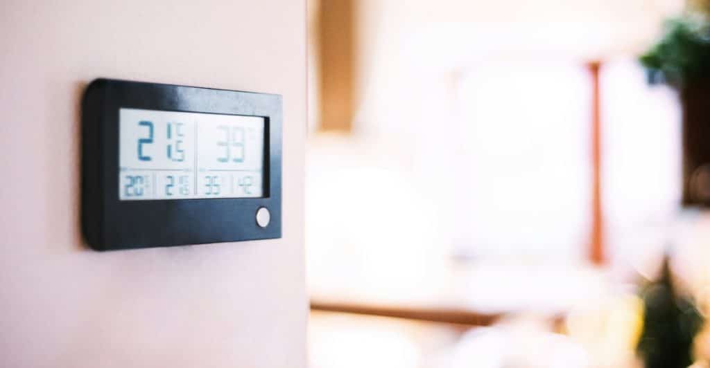 A digital thermostat showing temperature readings on a light-colored wall.