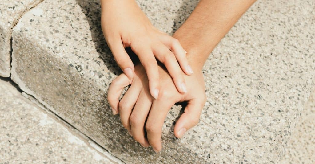 Two hands, one appearing to be a man's and one a woman's, clasped together on a light-colored, textured surface.