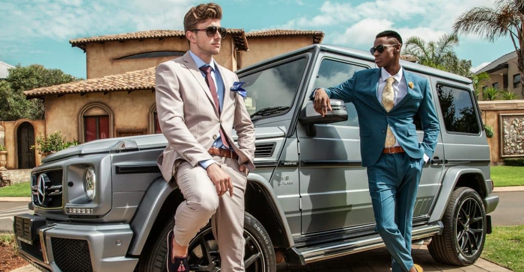Two men wearing suits leaning on a car.