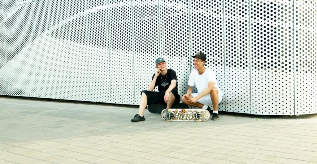 Two men sitting on skateboards outdoors, casually talking and laughing.