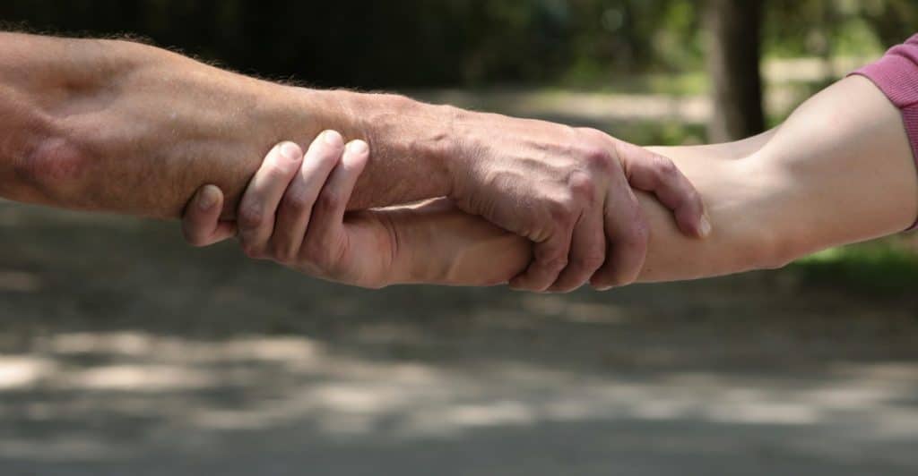 Two people are grasping each other's forearms tightly outdoors.