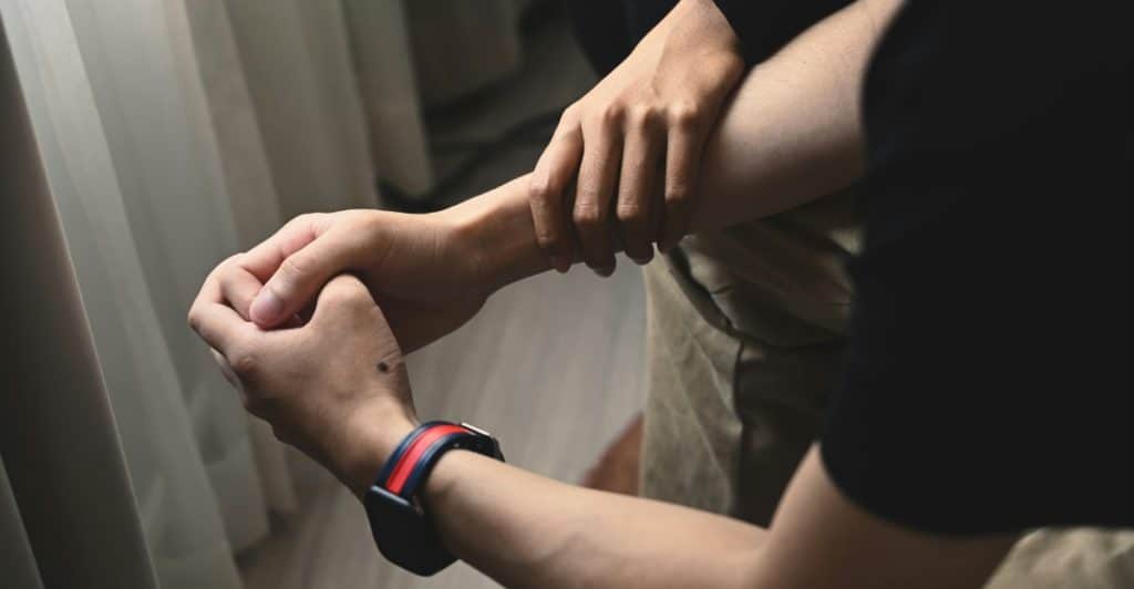 One person's hands are gently holding another person's forearm.