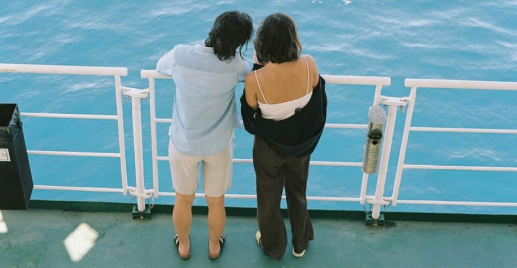 Two people are standing on a boat deck, looking out at the ocean.