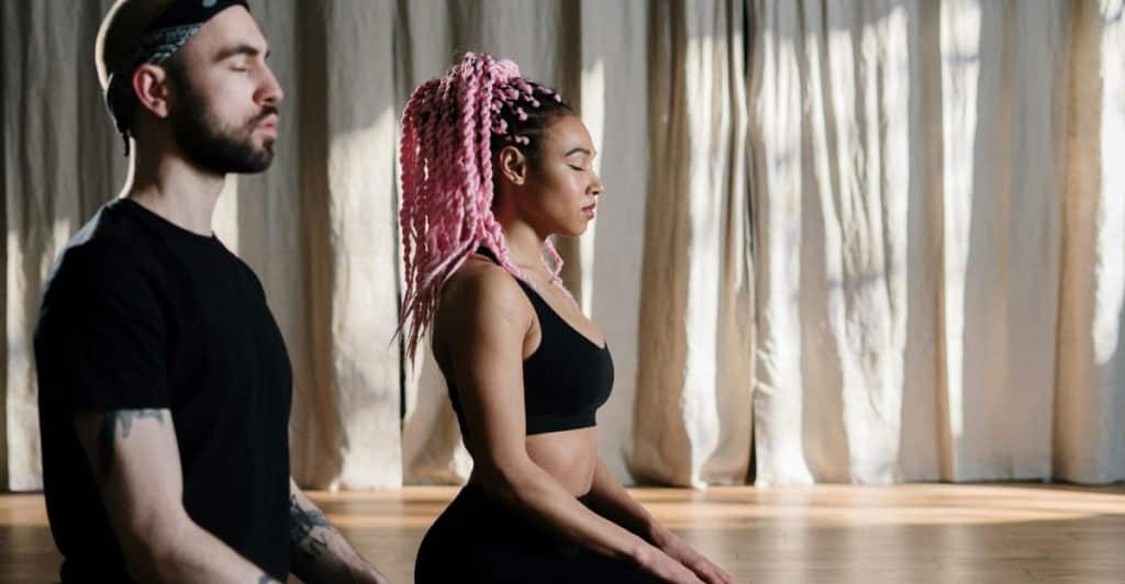 A man and a woman sitting on the floor with their eyes closed in a meditative posture.