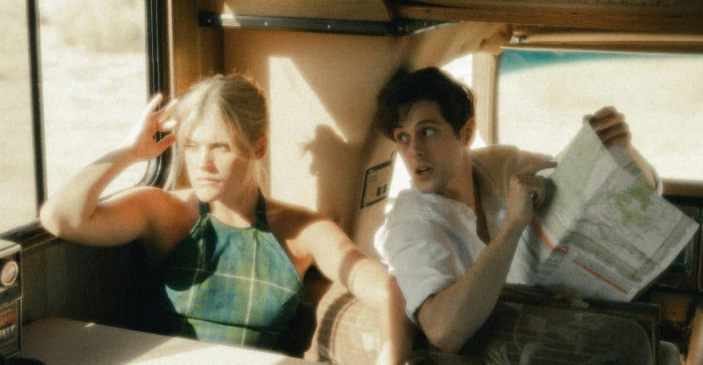 A person with blonde hair wearing a green and white plaid top looking to the left and a person with dark hair holding a map looking to the right while sitting in a vehicle