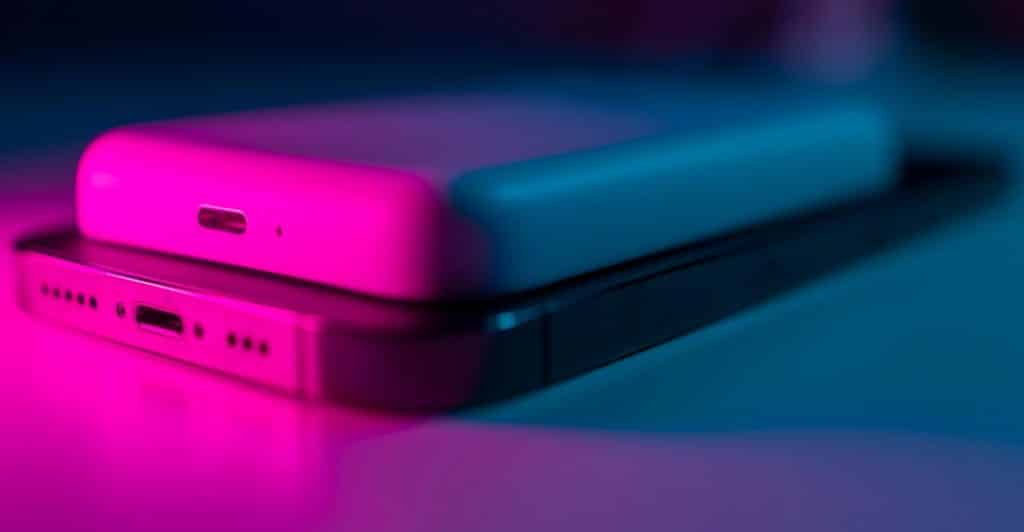 Two power banks stacked on top of a smartphone, illuminated by vibrant pink and blue ambient lighting