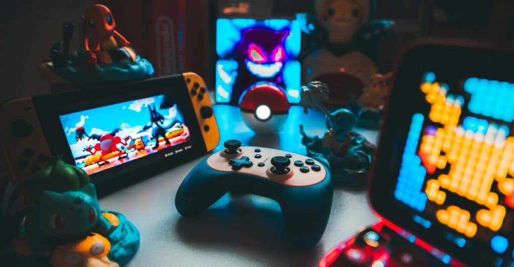 A collection of video game memorabilia including a Nintendo Switch console, a blue Nintendo Switch Pro Controller, Pokémon figurines, and other glowing gaming accessories.