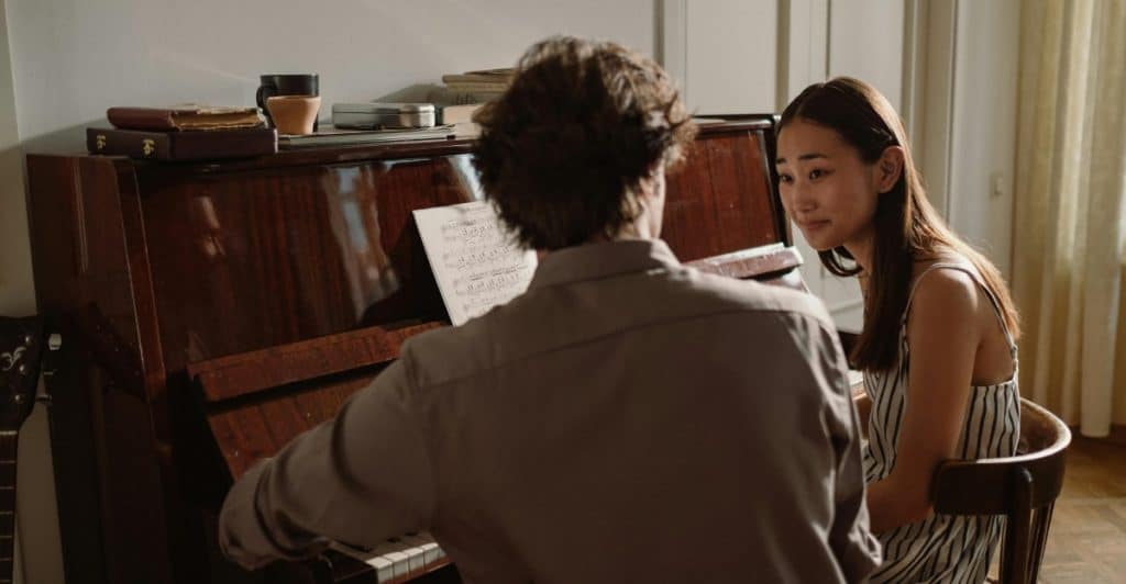 A woman sitting and attentively listening to a man playing the piano