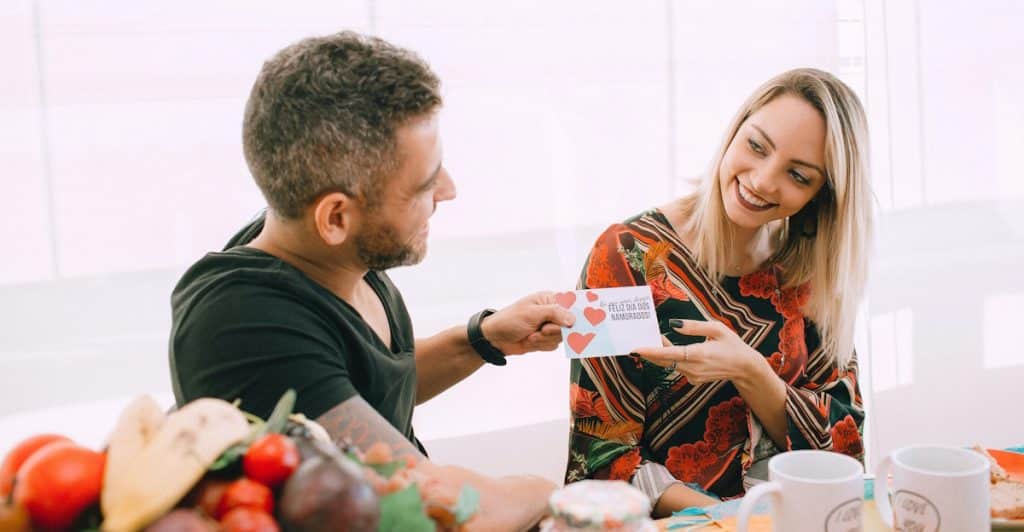 A woman smiling as a man hands her a small card with hearts on it.