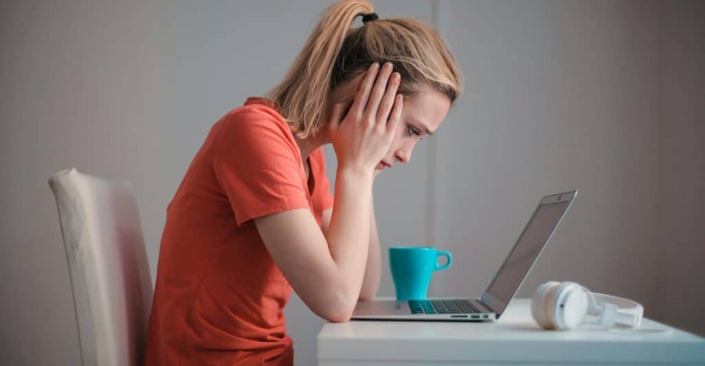 A woman sitting at a table with a laptop, her head in her hands, appearing stressed or overwhelmed.
