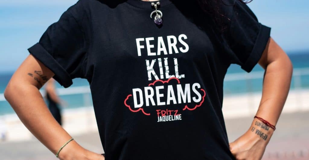 A woman from the chest down wearing a black t-shirt that says "FEARS KILL DREAMS".