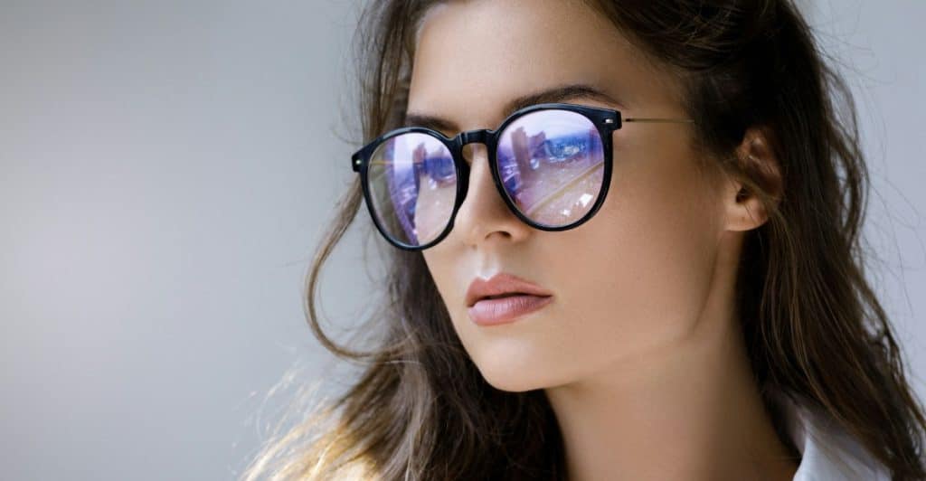 A woman with long hair wearing round, dark-rimmed blue light filtering glasses.