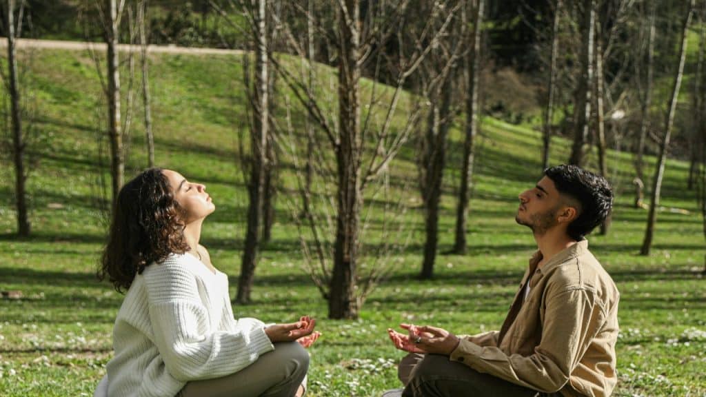 A couple  sits in a relaxed position, eyes closed, using breathwork to regulate their  emotions.