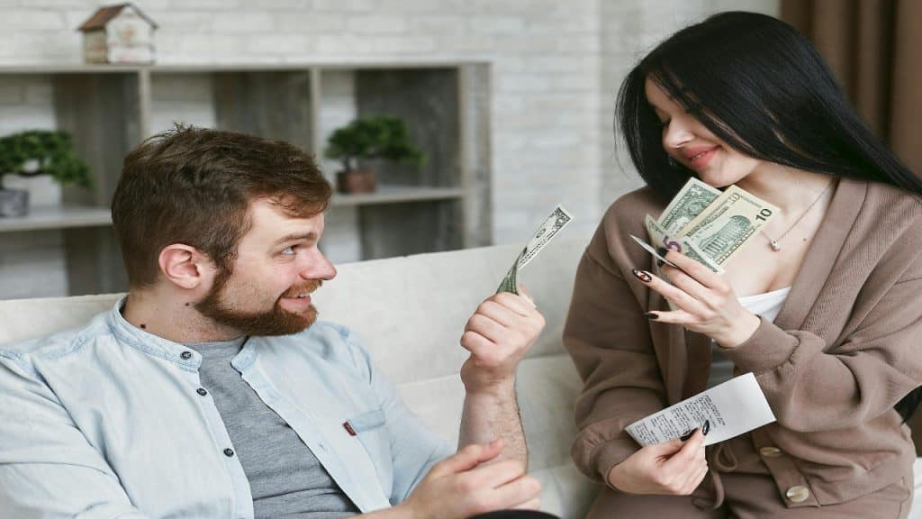 A happy couple sitting on a couch having an open conversation about money in the living room.