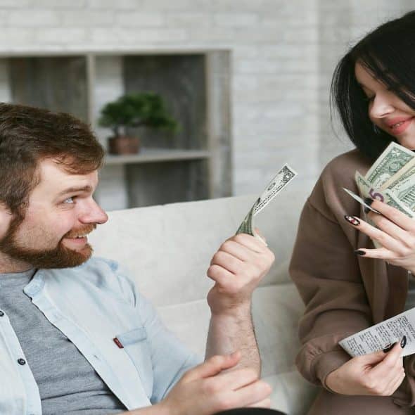 A happy couple sitting on a couch having an open conversation about money in the living room.