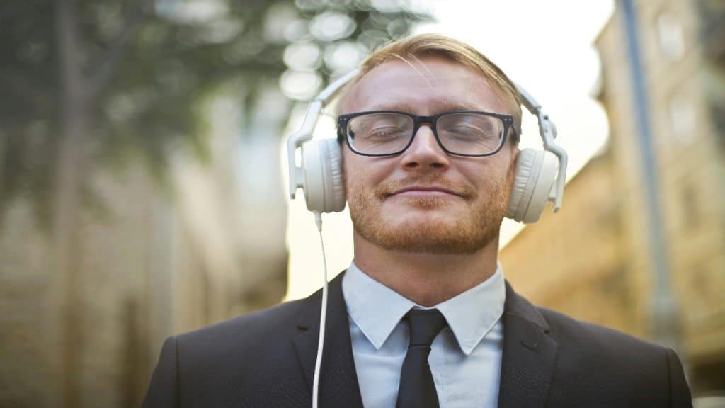 A smiling man walking outdoors, headphones on, clearly content