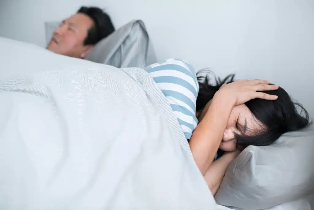 A lady covering her ears because of his snoring husband