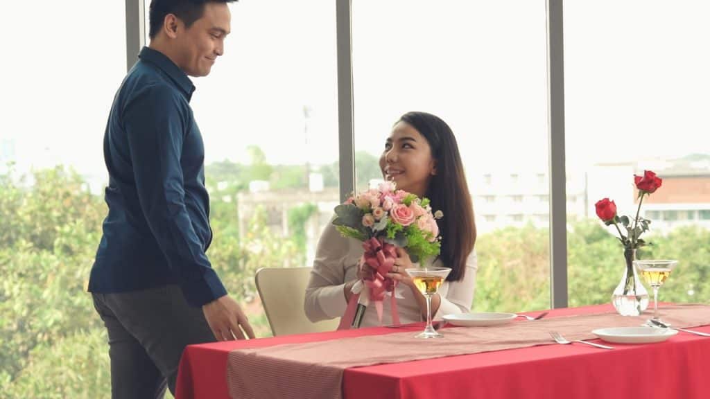 A man treats his partner to a restaurant and gives her a bouquet of flowers.