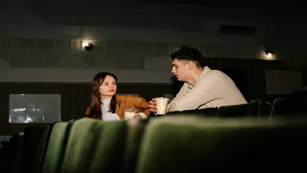 A couple holds a cup of popcorn as they watch a movie together.