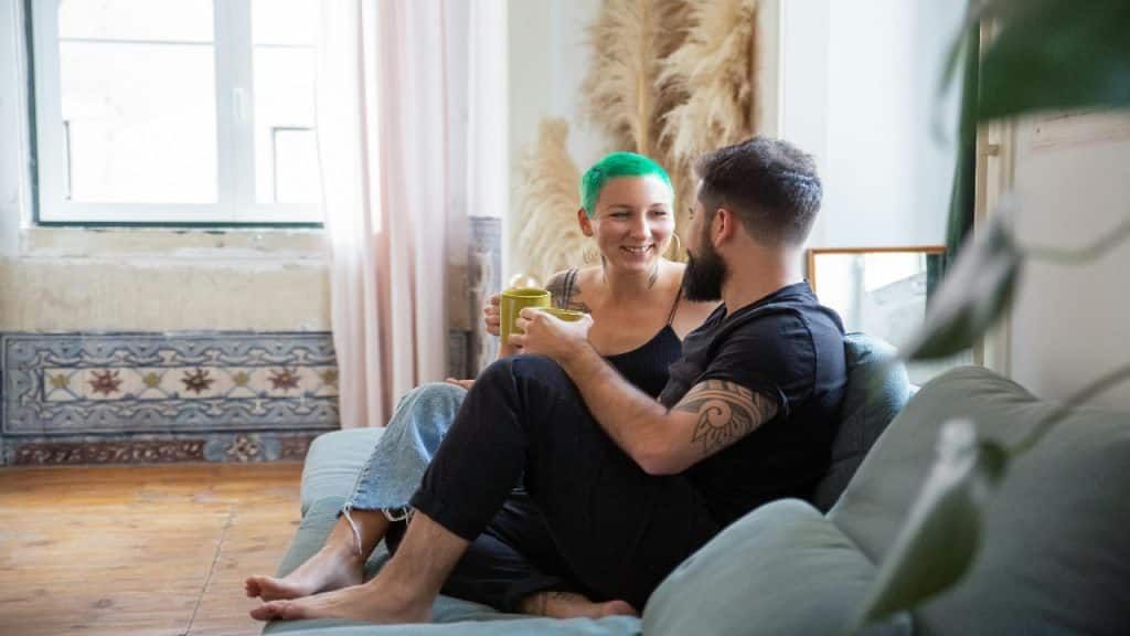 A couple sits on the living room floor, enjoying a casual emotional check in over coffee.