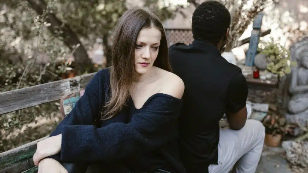 A couple sits apart on a bench, emotionally disconnected.