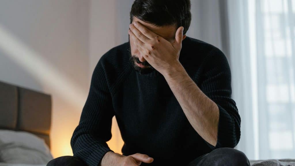 A man sits on the bed  in a quiet room, processing emotional stress.
