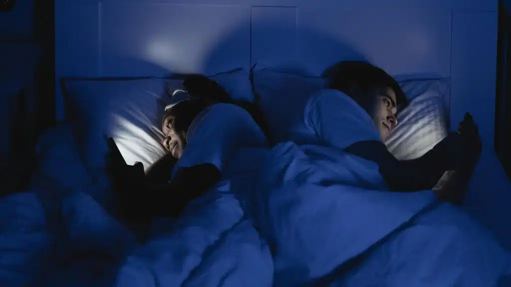 A couple lying in bed facing opposite directions, no physical contact.