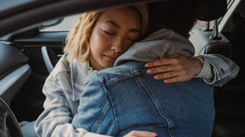 A stressed man sitting in silence while his partner cuddles him showing  concern.