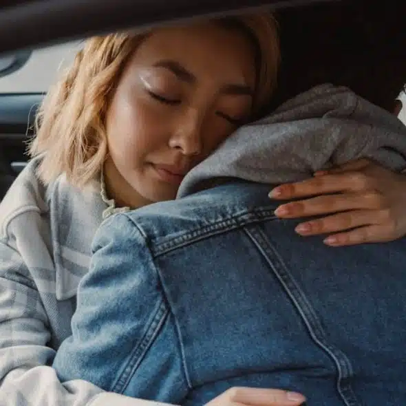 A stressed man sitting in silence while his partner cuddles him showing  concern.