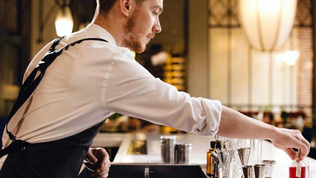 Man in his 30s mixing a cocktail at home, with modern bar tools and soft ambient lighting in a stylish kitchen.