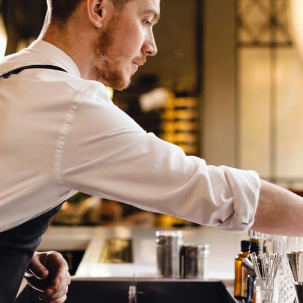 Man in his 30s mixing a cocktail at home, with modern bar tools and soft ambient lighting in a stylish kitchen.