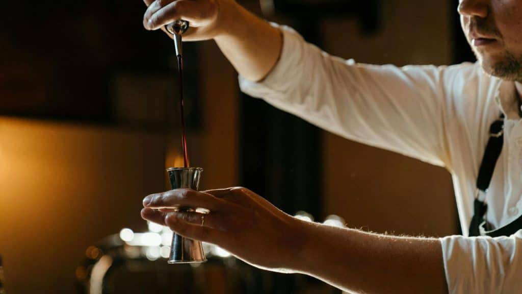 Man carefully measuring alcohol into a jigger over a mixing glass, concentrating while preparing a cocktail.