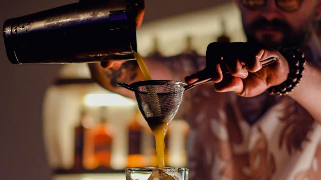 Stylish home bar corner featuring matte black bar tools, glassware, spirits, and warm LED shelf lighting.