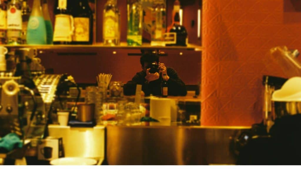 A man capturing a slow motion video of a drink in a well lit modern kitchen.
