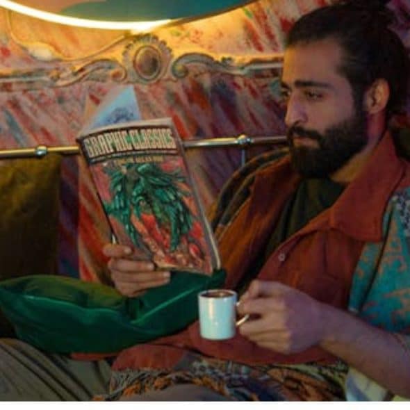 Man in casual style reading hardcover graphic classics at home.