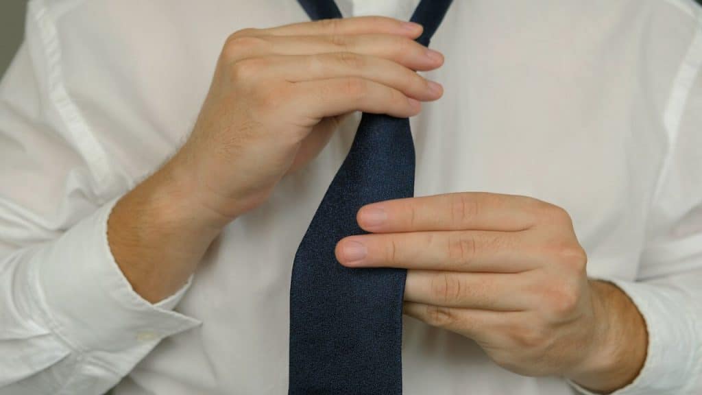 A man in white shirt tying a blue tie.