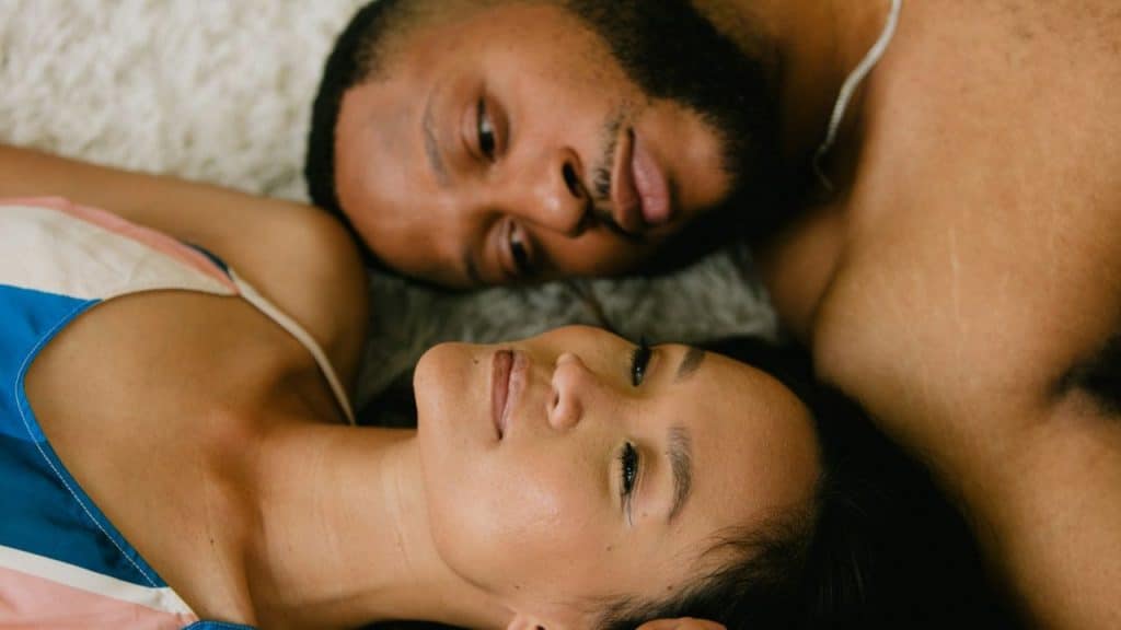 A man and woman lie side-by-side, looking at each other.