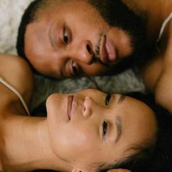 A man and woman lie side-by-side, looking at each other.