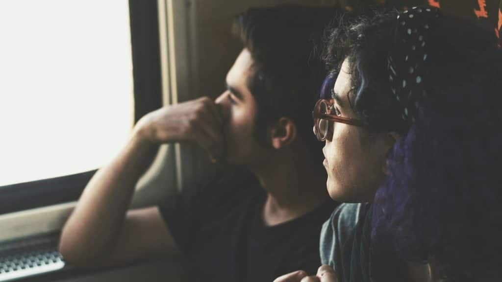 A couple looks out a window, the woman with purple hair in the foreground.