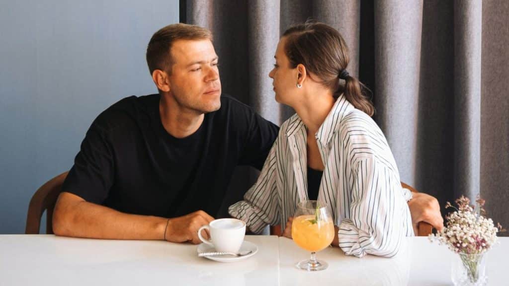 A man and woman gaze at each other across a table with drinks and flowers.