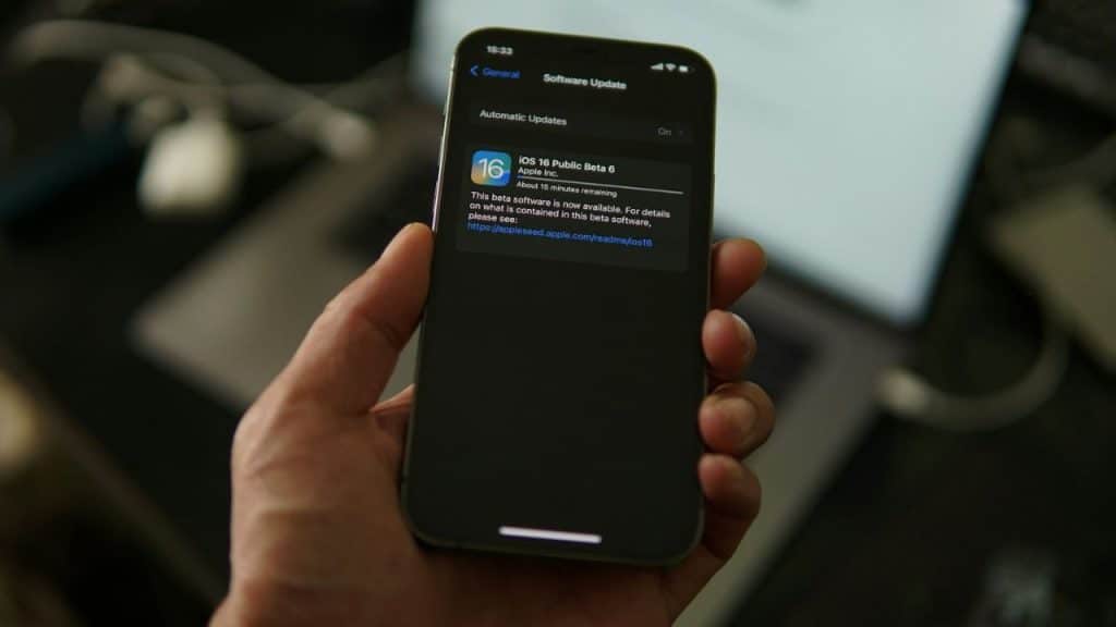 A hand holds an iPhone displaying a software update notification for iOS 16 Public Beta 6.