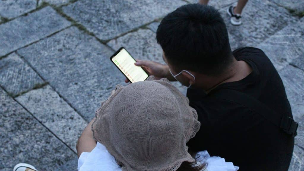 An overhead view shows two people looking at a smartphone screen, sitting on stone steps.
