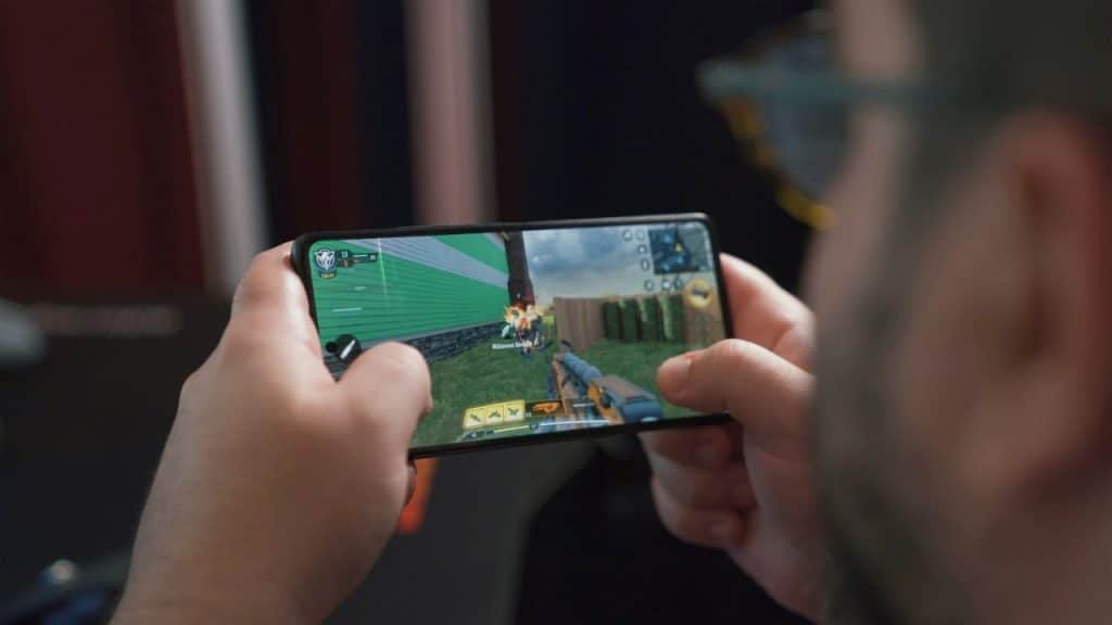 A person holds a smartphone horizontally, playing a first-person shooter game.