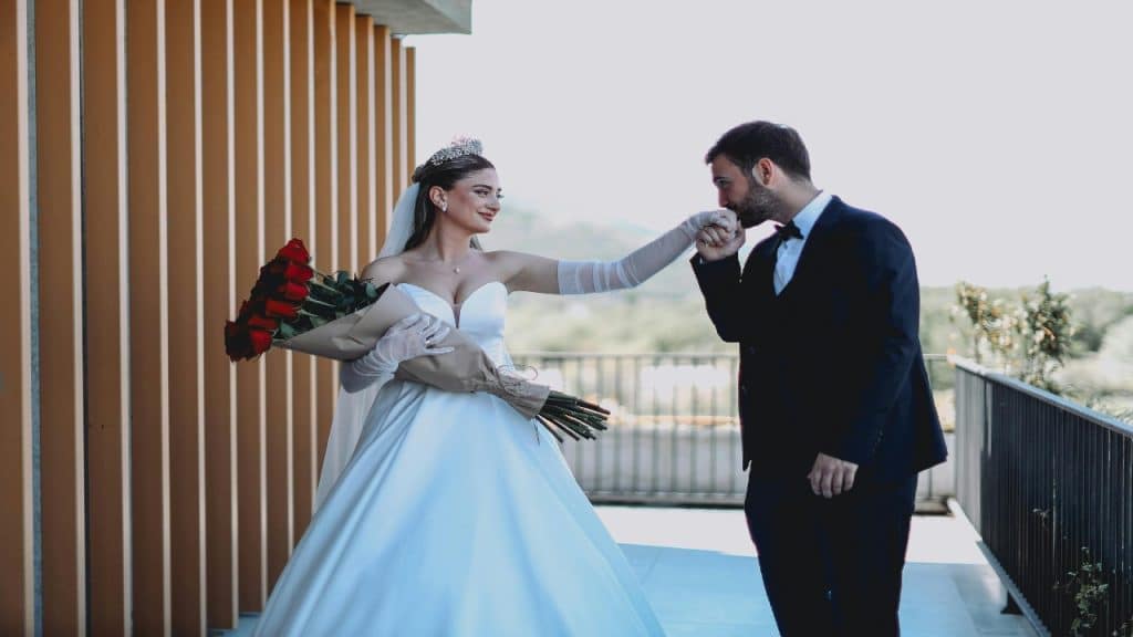 A man gently kisses the hand of his bride, who is wearing a crown.