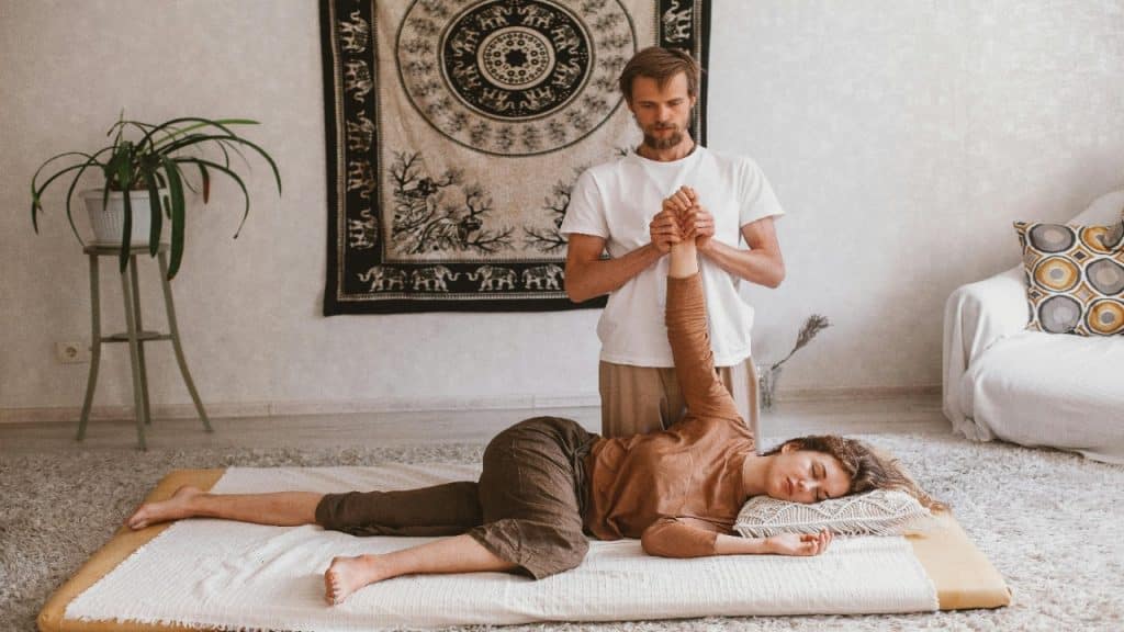 A man performs a therapeutic massage technique on a woman lying on a floor mat.