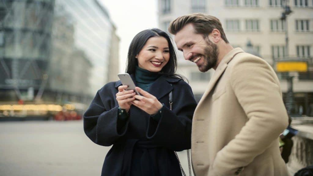 A smiling couple as the woman shows something on her phone to the man.