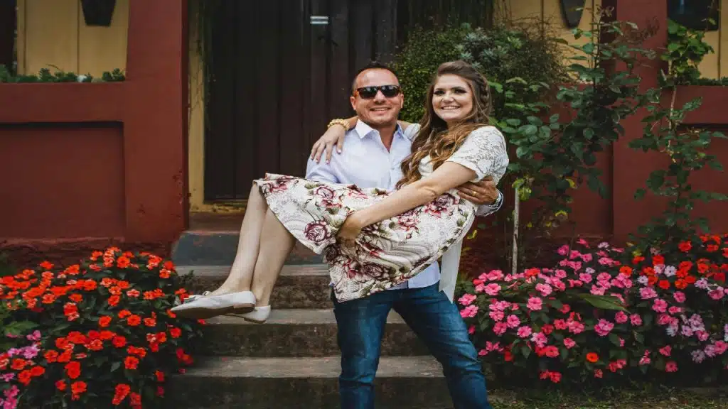 A smiling man joyfully carrying a woman in a floral dress.