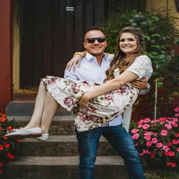 A smiling man joyfully carrying a woman in a floral dress.